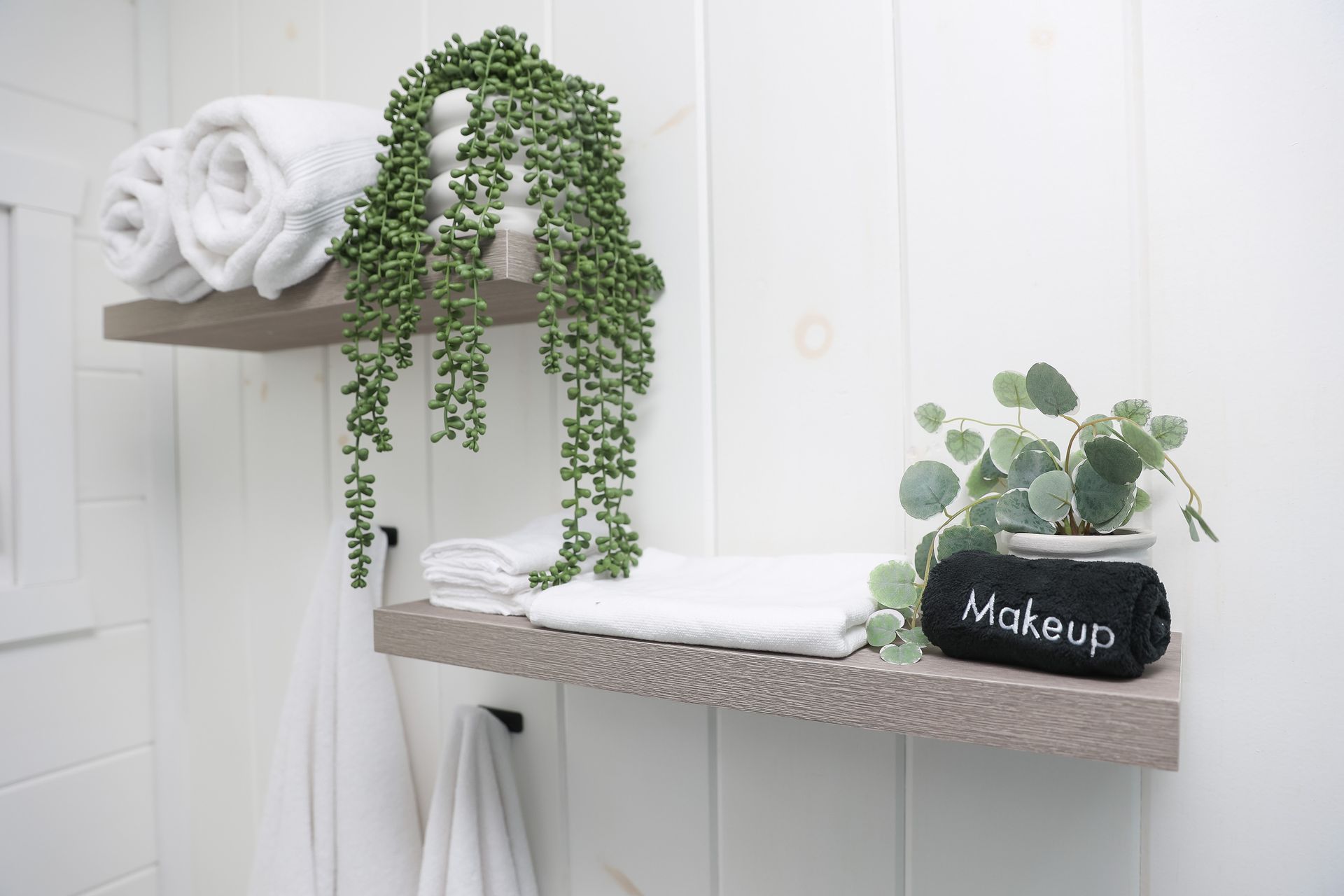 A bathroom shelf with towels , a plant and a makeup bag.
