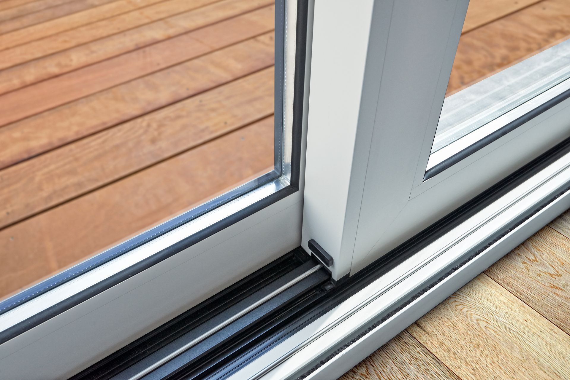 Close-up of sliding glass door track and frame beside wooden deck flooring.