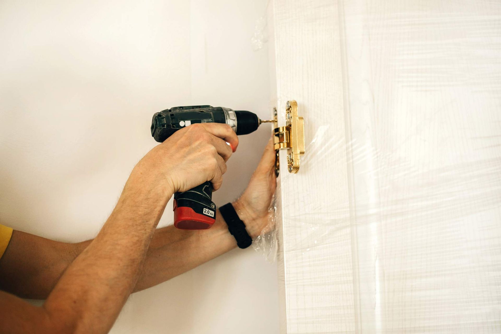 Door repair company technician using drill to fix gold door latch on white wooden door frame.