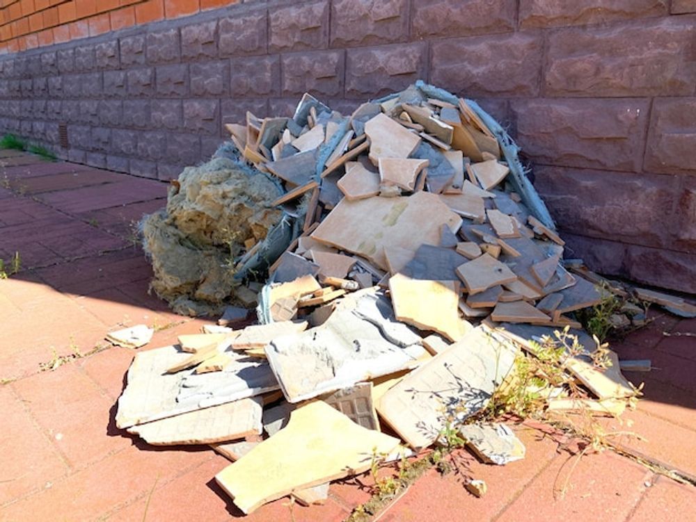 A pile of broken tiles is sitting on the sidewalk in front of a brick wall.