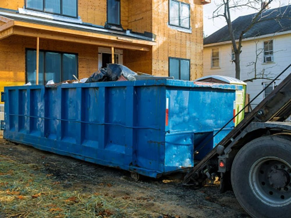 A blue dumpster is sitting in front of a house under construction.