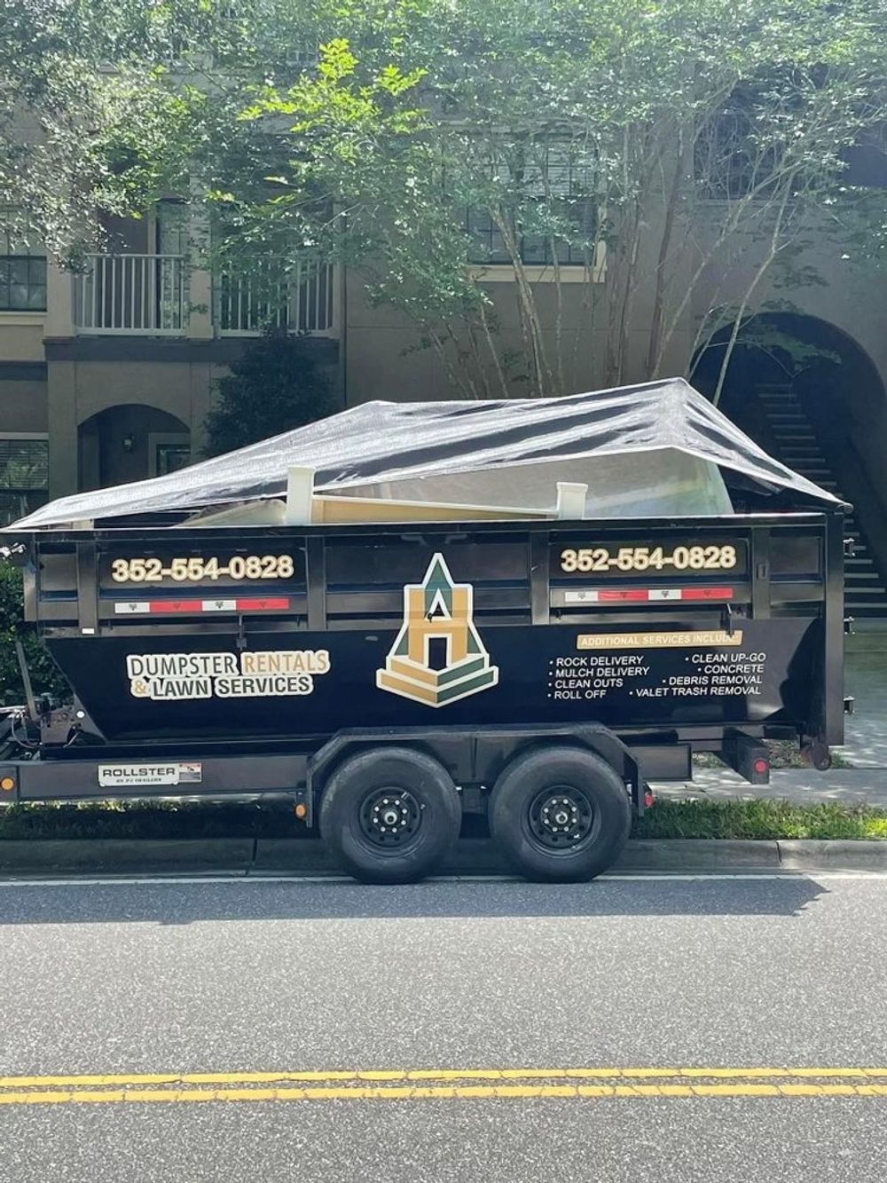 A dumpster on a trailer is parked on the side of the road.
