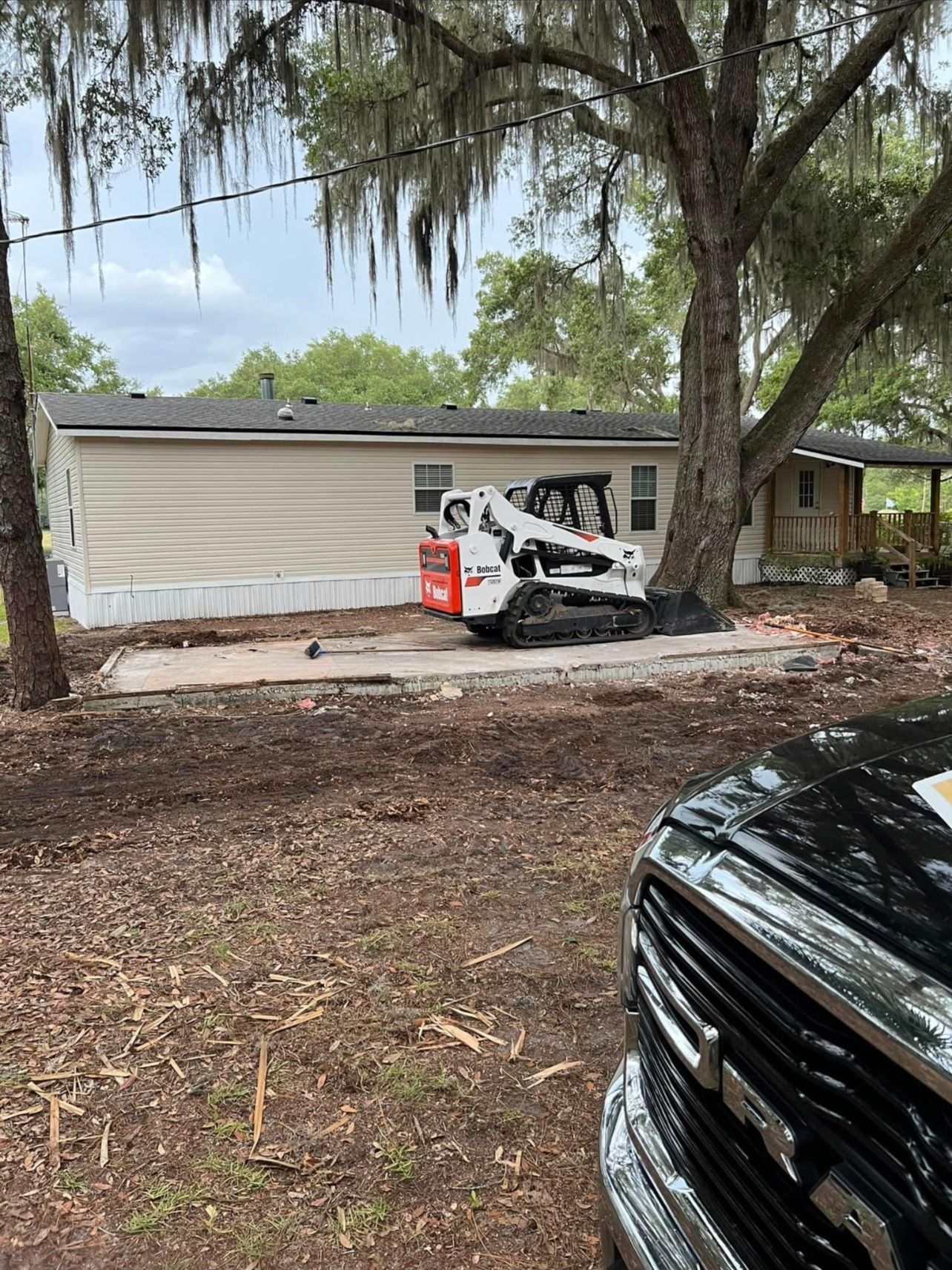 A bobcat is parked in front of a mobile home.