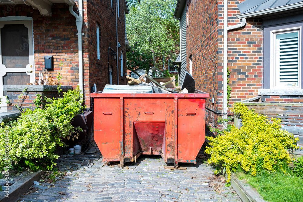 A red dumpster is parked in front of a brick house.