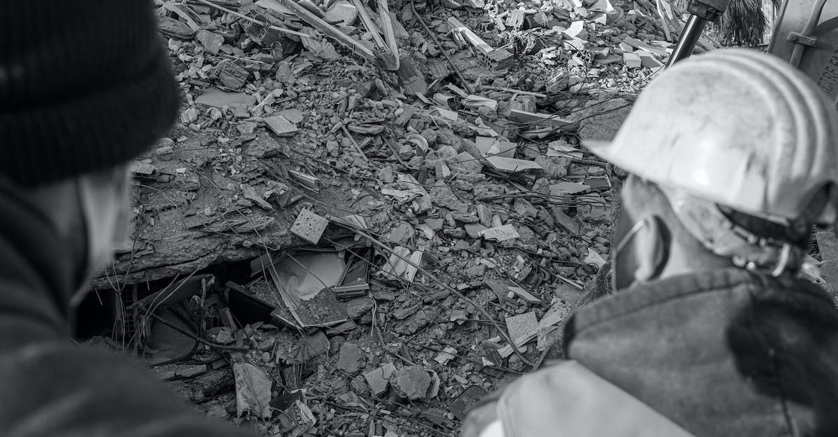 A black and white photo of two people looking at something in the woods.