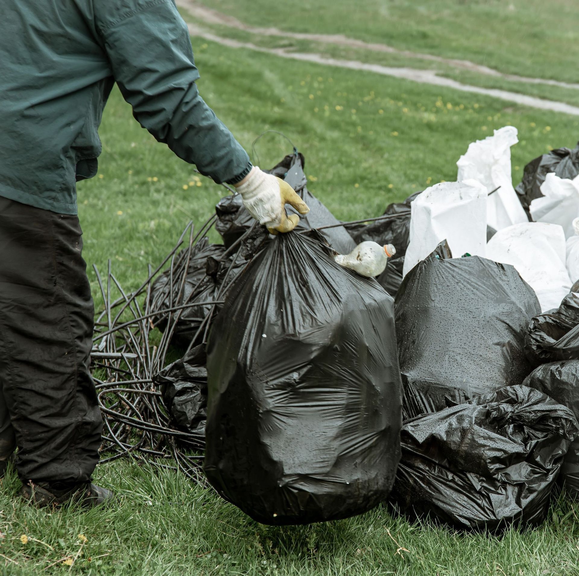 A man is holding a black garbage bag in front of a pile of garbage bags.