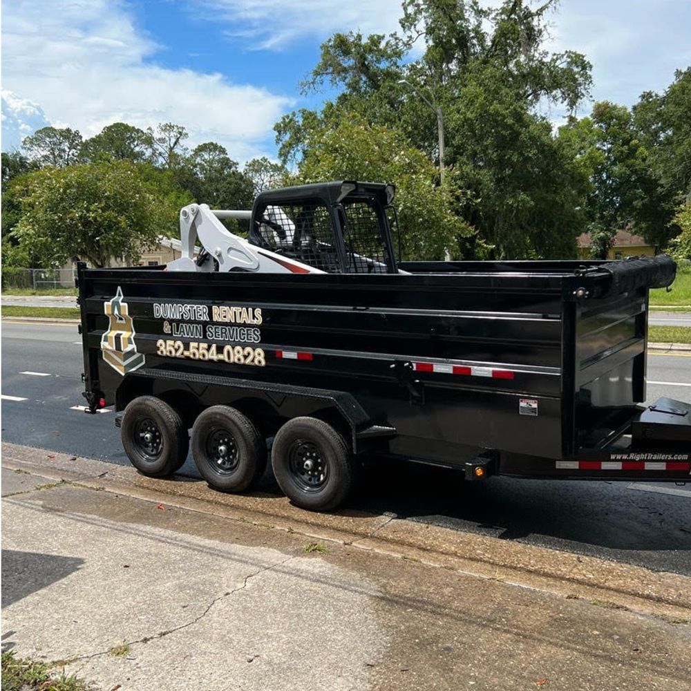 A dumpster trailer with a bobcat on it is parked on the side of the road.