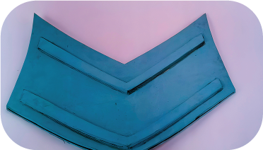 Protector de esquinas de goma de color azul, en forma de V, con tres crestas elevadas sobre una superficie rosa.