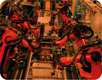 Robots industriales, brazos naranjas, ensamblando componentes en un entorno de fábrica.