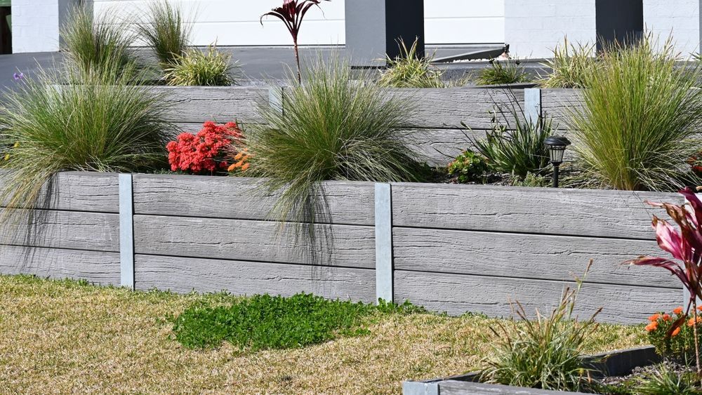 A wooden retaining wall with plants and flowers in front of a house — CQ Fencing & Retaining Walls In Clinton, QLD