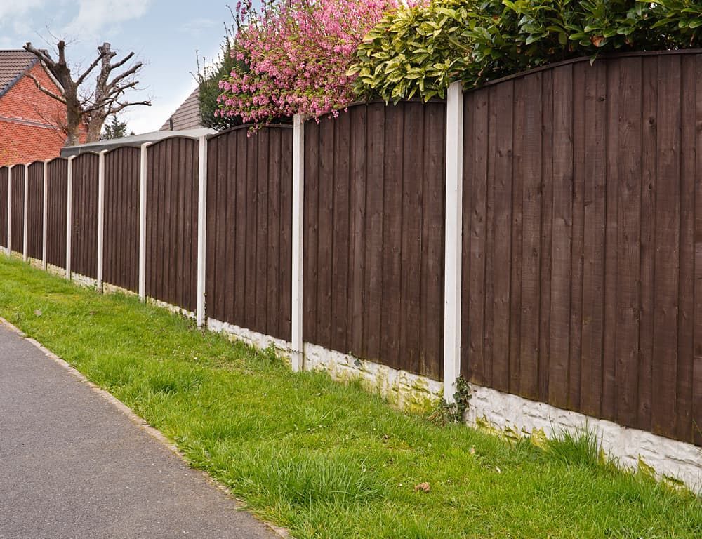 A Wooden Fence Surrounds a Lush Green Field Next to A Road — CQ Fencing & Retaining Walls In Clinton, QLD