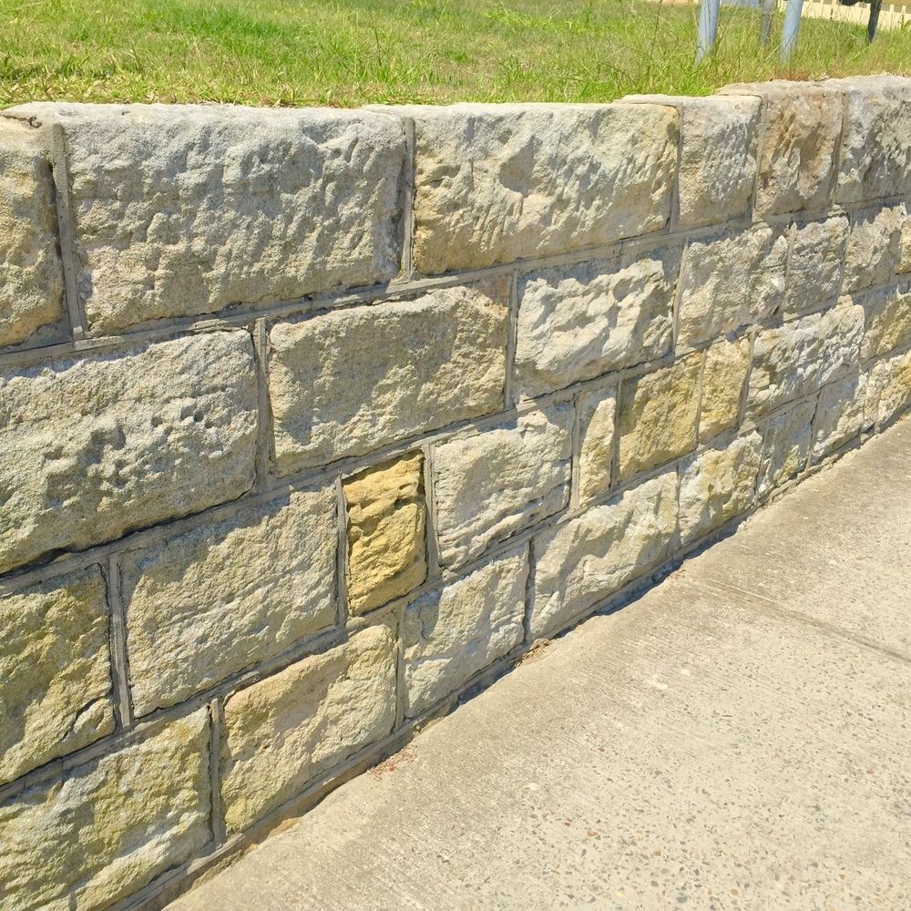 Stone Retaining Wall Next to A Concrete Walkway and Grass, with Various Beige and Yellow Tones — CQ Fencing & Retaining Walls In Rockhampton, QLD