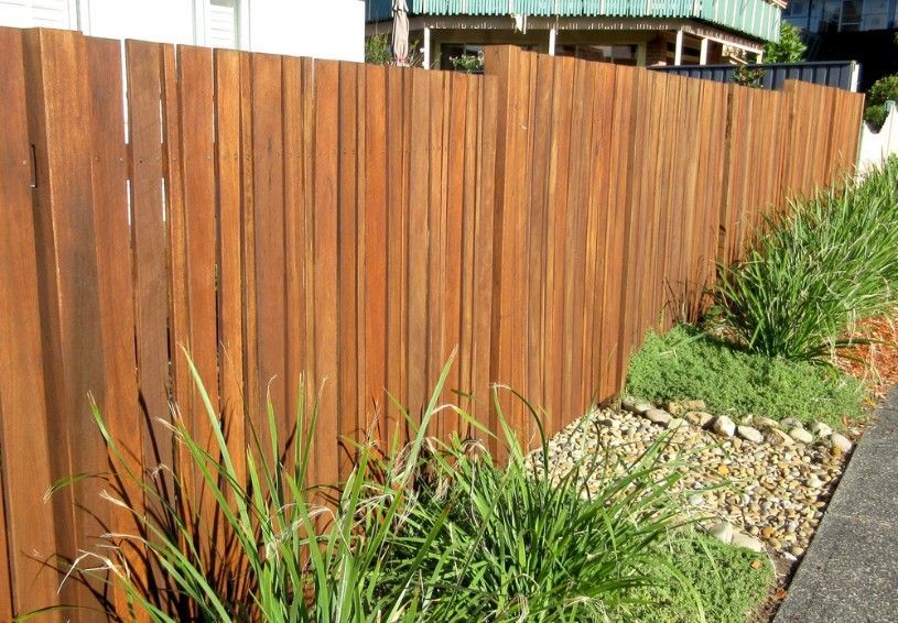 A Wooden Fence Is Surrounded By Grass And Rocks Next To A Sidewalk — CQ Fencing & Retaining Walls In Clinton, QLD