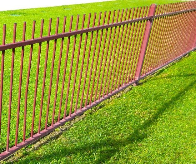 A Red Metal Fence Surrounds A Lush Green Field — CQ Fencing & Retaining Walls In Clinton, QLD