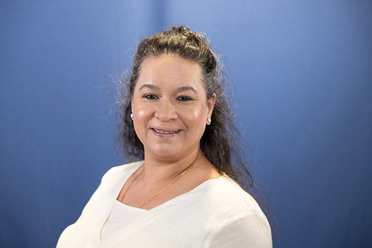 A woman in a white shirt is smiling in front of a blue background.