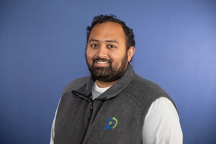 A man with a beard is wearing a vest and smiling for the camera.