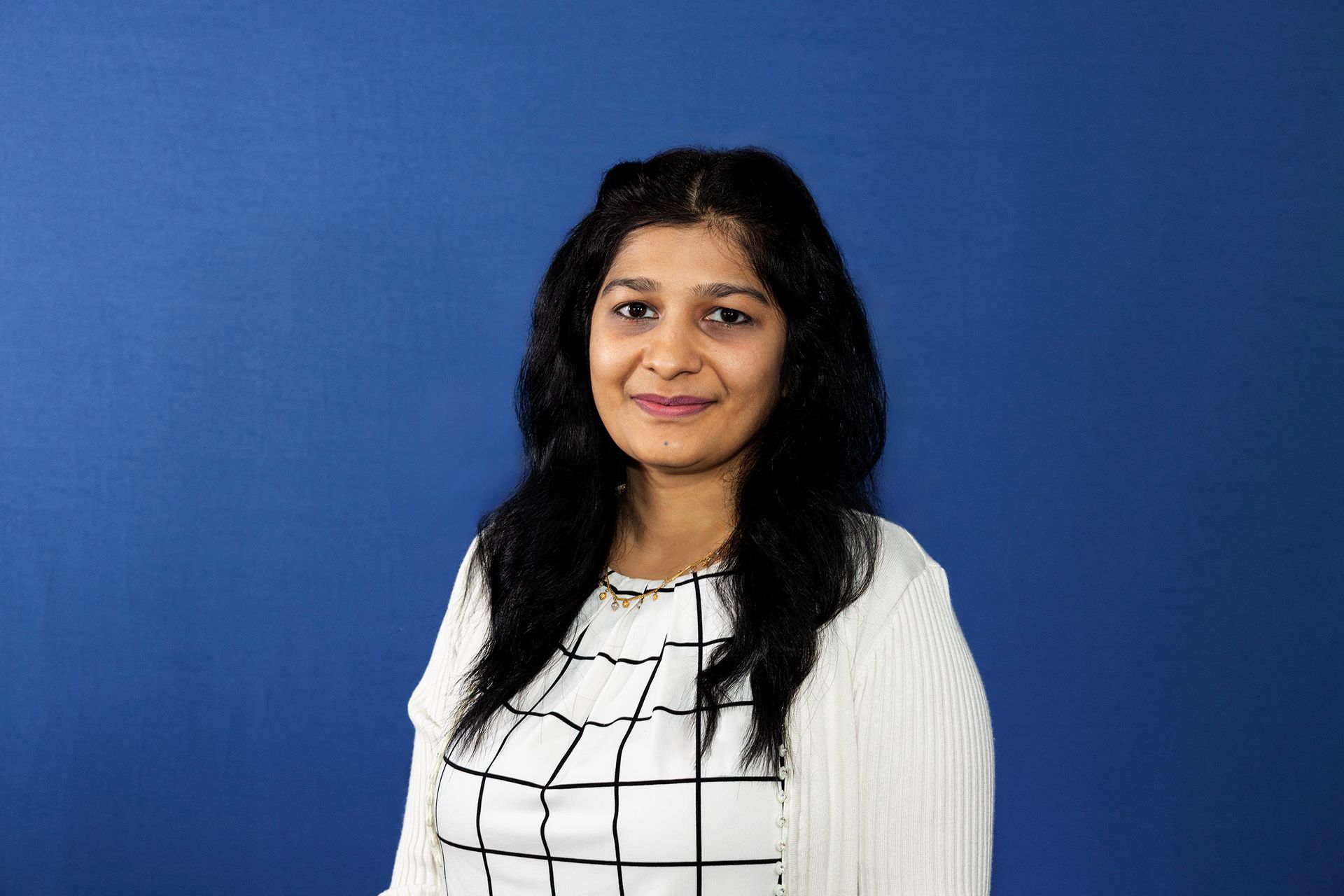Woman with dark hair and light skin smiles against a blue backdrop.