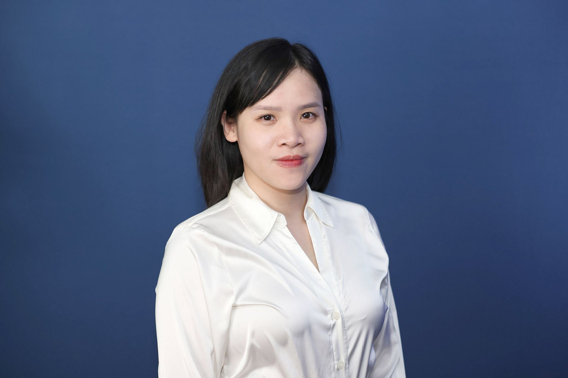 Woman with dark hair in a white shirt smiles against a blue background.