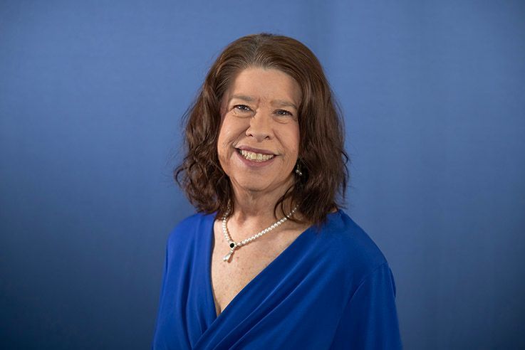 A woman in a blue dress and necklace is smiling for the camera.