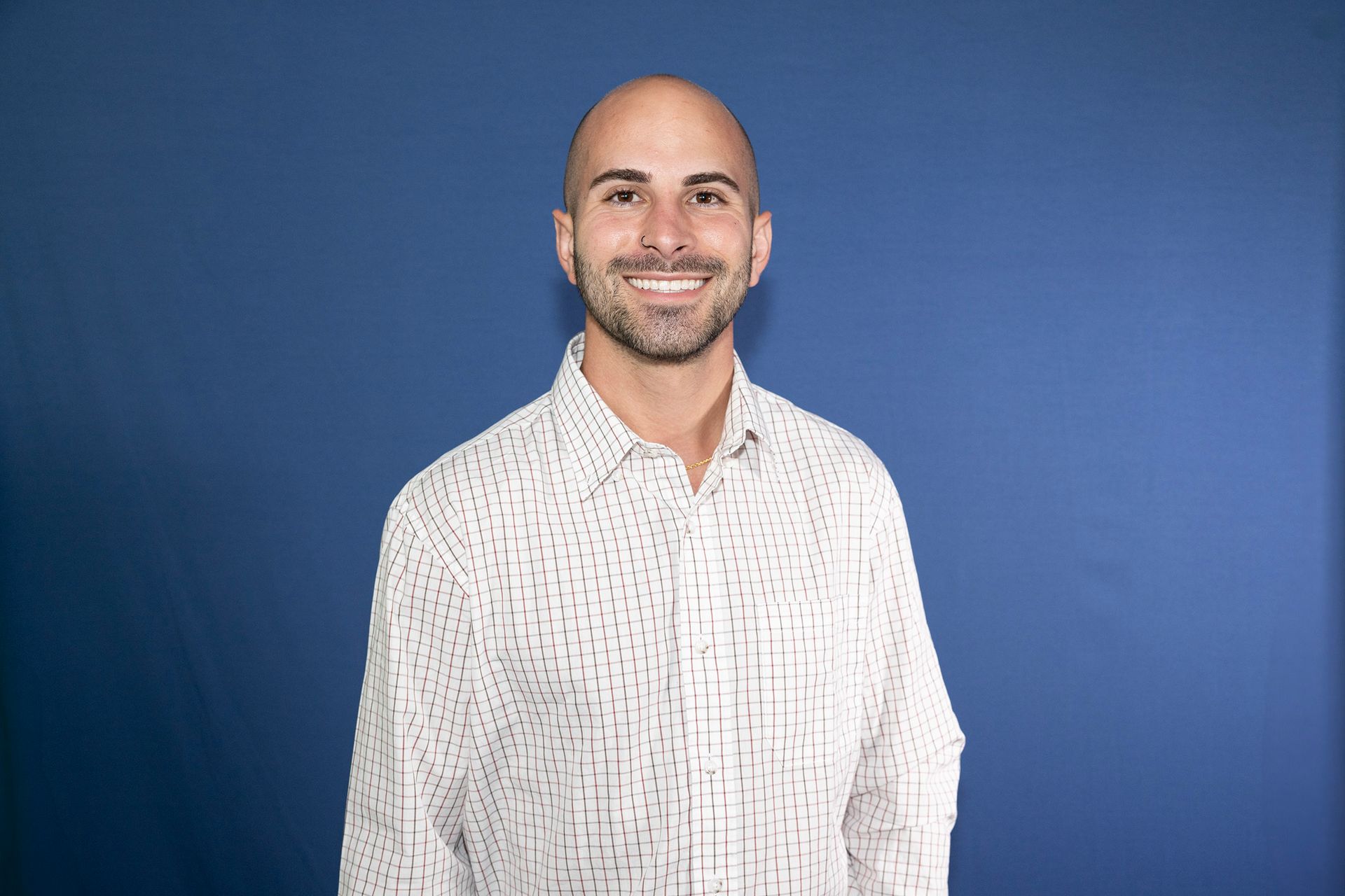 A bald man with a beard is smiling in front of a blue wall.