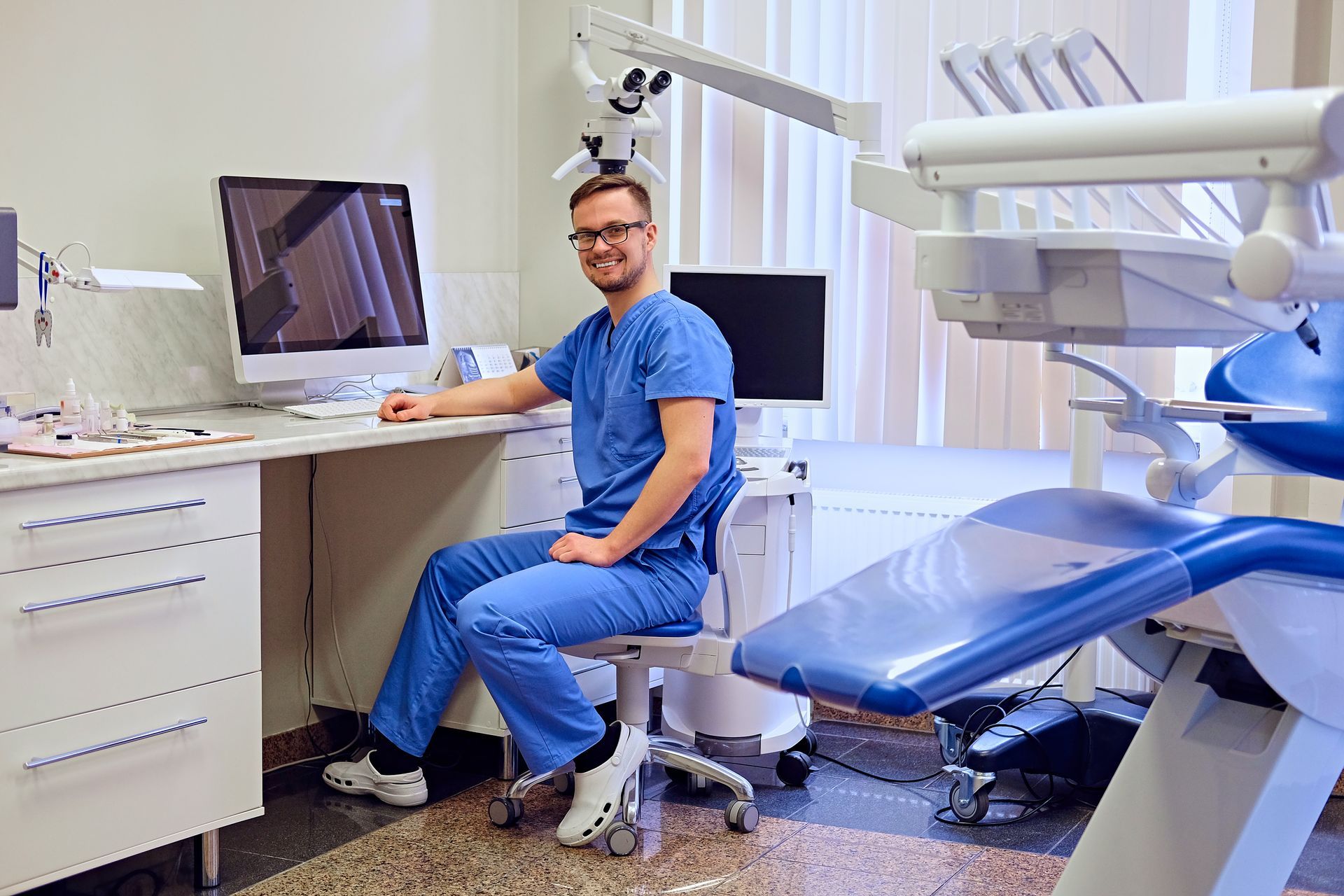 Dentist in blue scrubs smiles while sitting at a desk with Pro-Fi 20/20 Dental CPAs in Suwanee, GA 