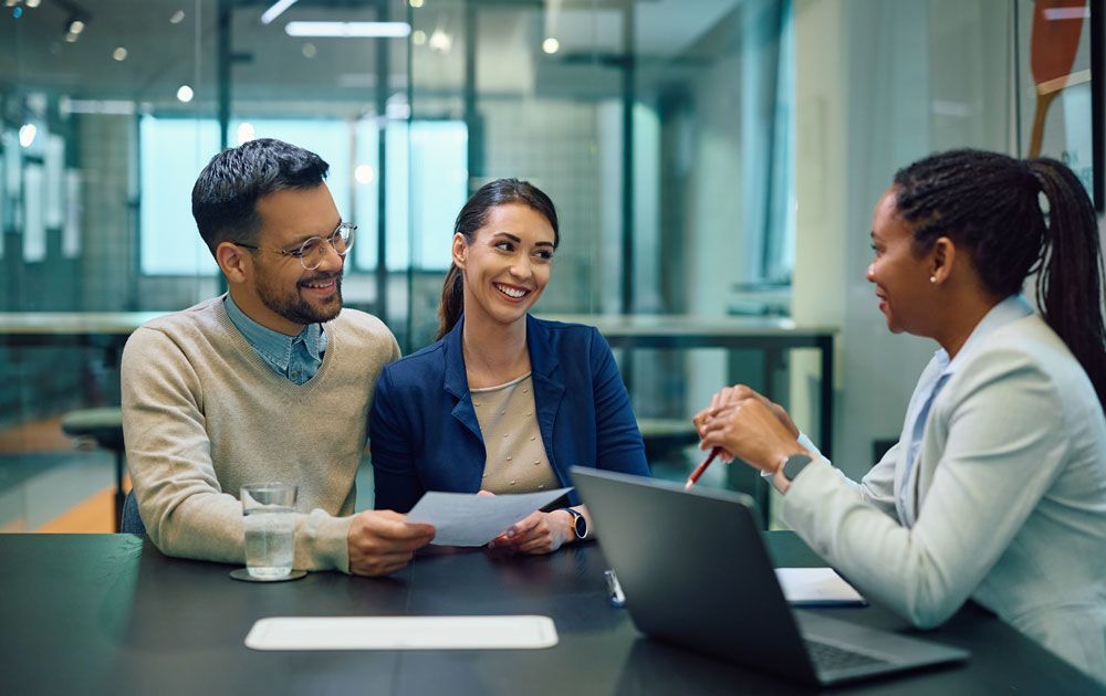 A man and woman are sitting at a table talking to a woman.