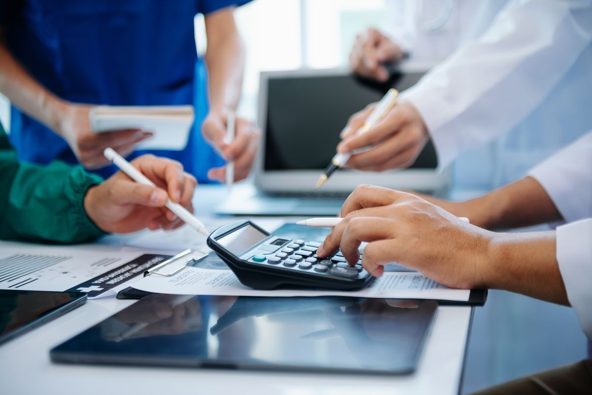 Hands using a calculator and pens over documents in a business meeting