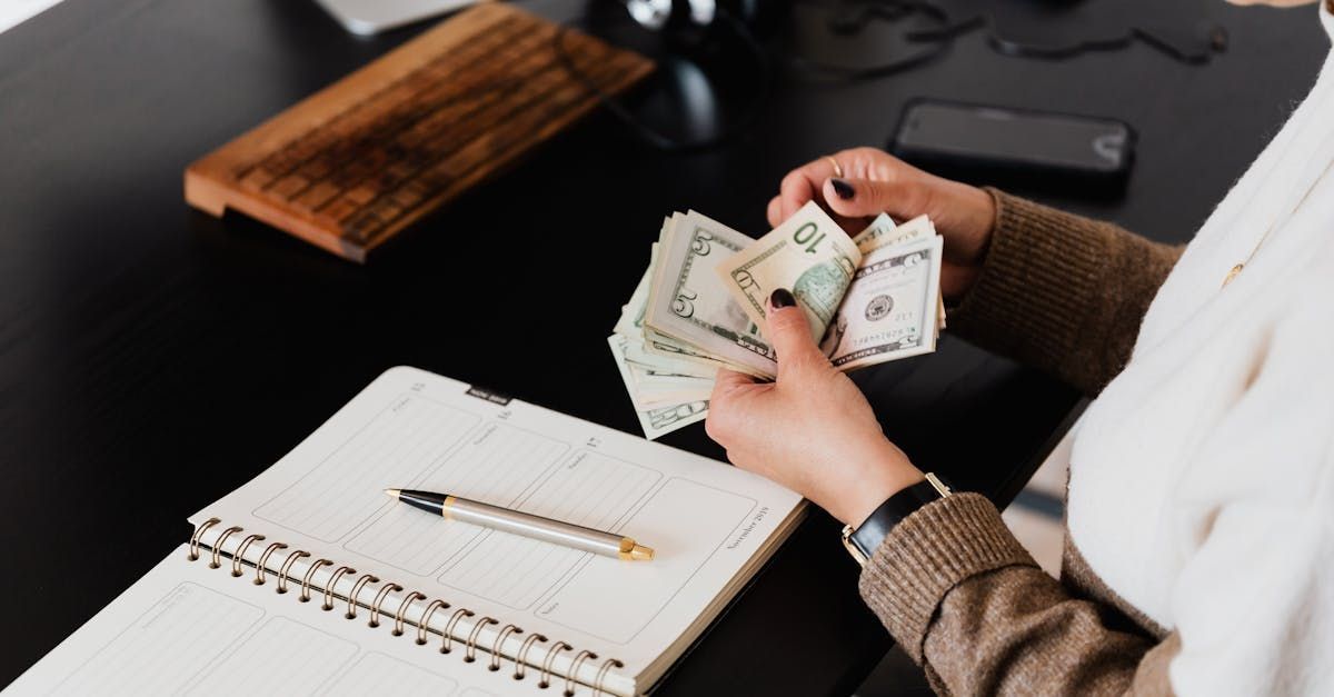 A woman is sitting at a desk holding a bunch of money in her hands.