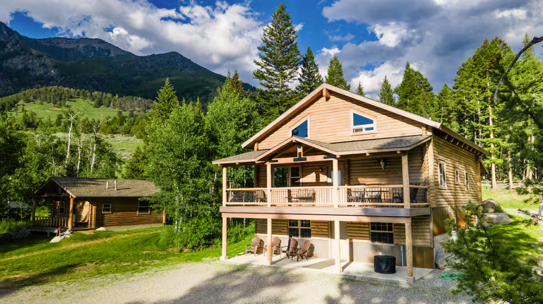 A large log cabin in the middle of a forest with mountains in the background.