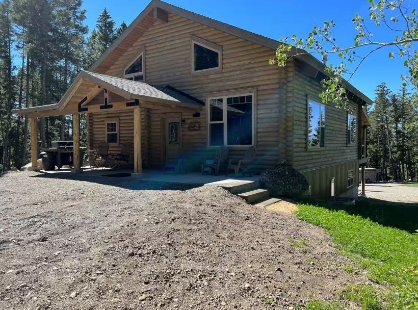 A log cabin is sitting on top of a dirt hill in the middle of a forest.