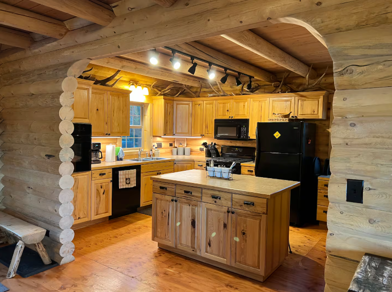 A kitchen in a log cabin with wooden cabinets and a black refrigerator.