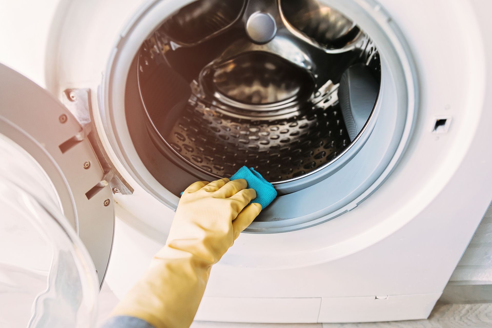 A person is cleaning a washing machine with a sponge.