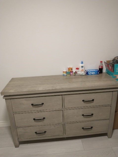 A dresser with six drawers is sitting in a room next to a wall.