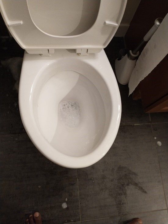 A white toilet sits on a tiled floor next to a toilet brush