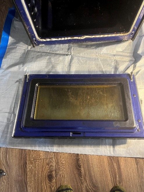 A dirty oven door is sitting on a wooden floor.