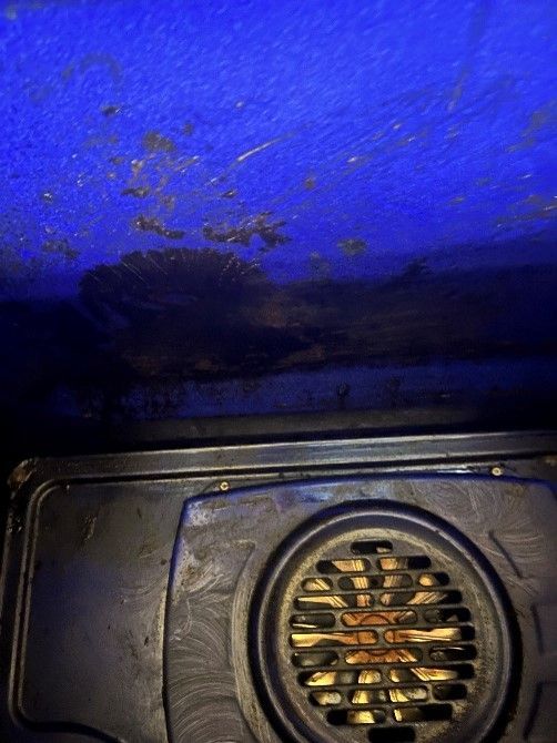 A close up of a dirty oven with a blue ceiling.