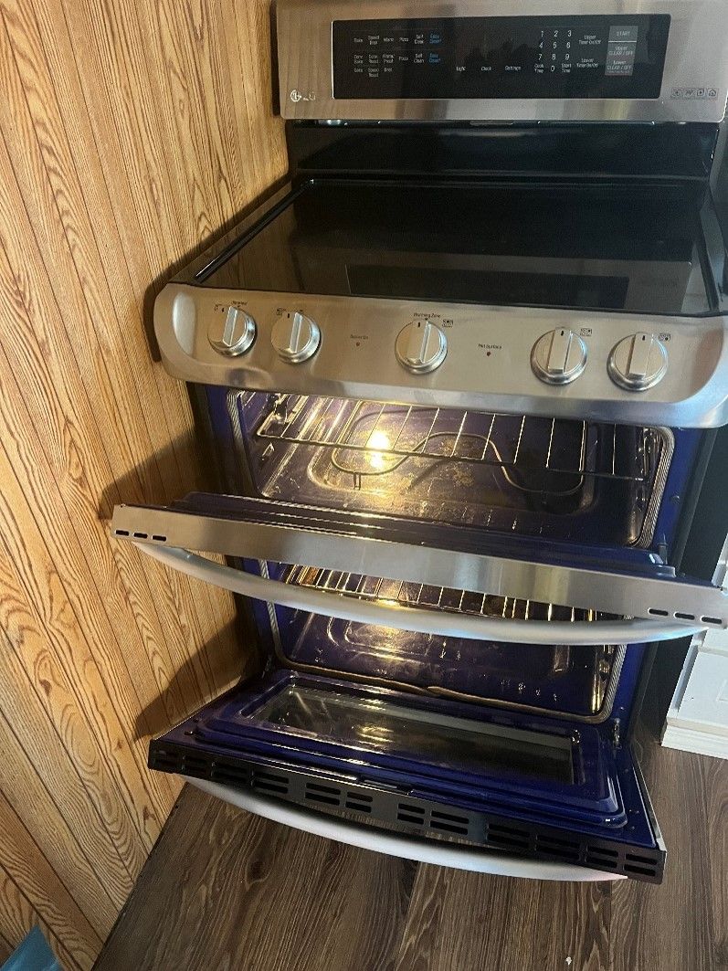 A stainless steel stove with the door open is sitting on top of a wooden table.