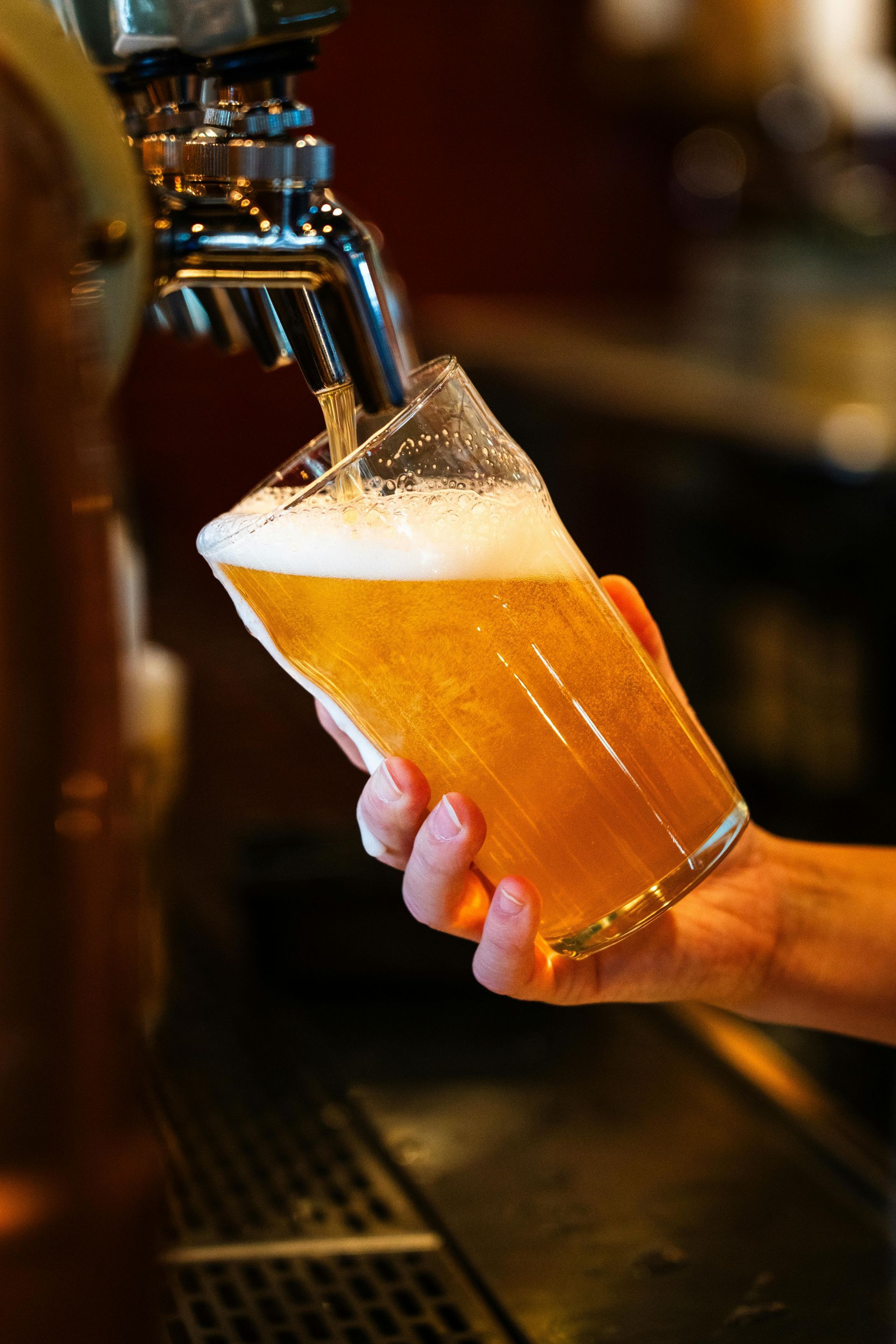 Pouring beer from tap into a glass; foamy head, golden liquid.