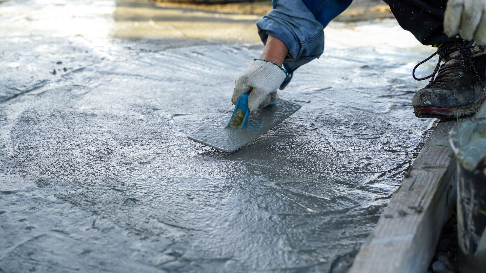 Worker smoothing wet concrete with a trowel on a sidewalk edge