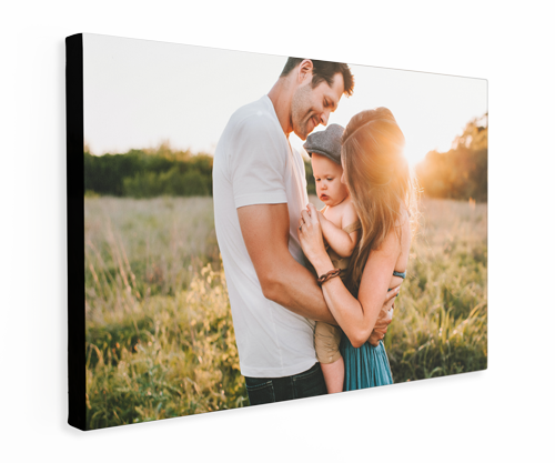 A man and a woman are holding a baby in a field with a setting sun.