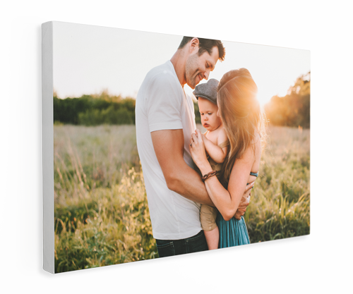 A man and a woman are holding a baby in a field with a setting sun.