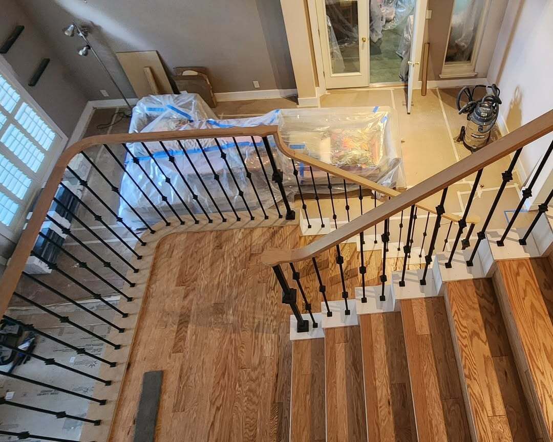 Staircase landing with wood steps, black balusters, and beige carpet runner in a house under renovation