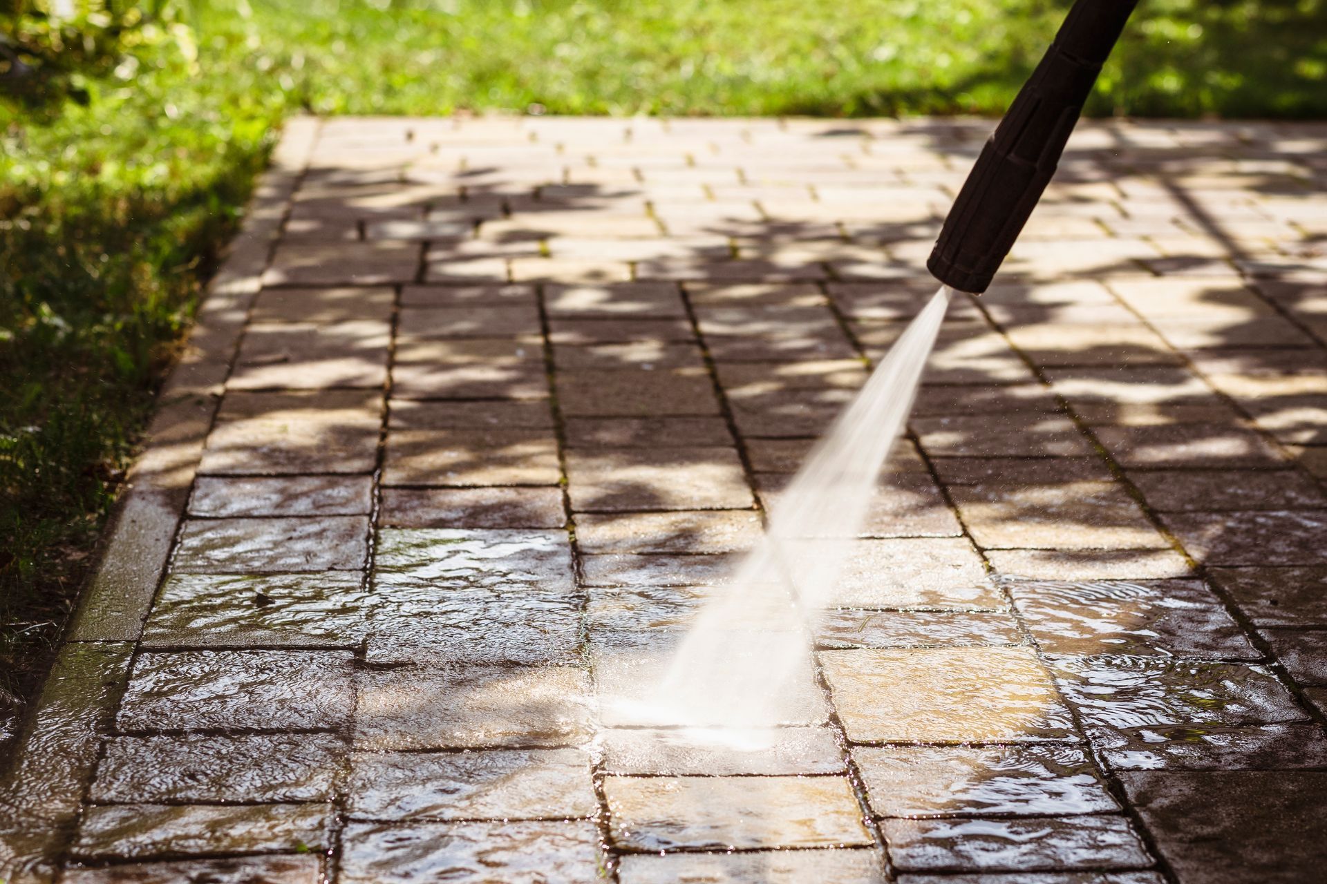 Pressure washing a brick patio with water spraying across the wet surface