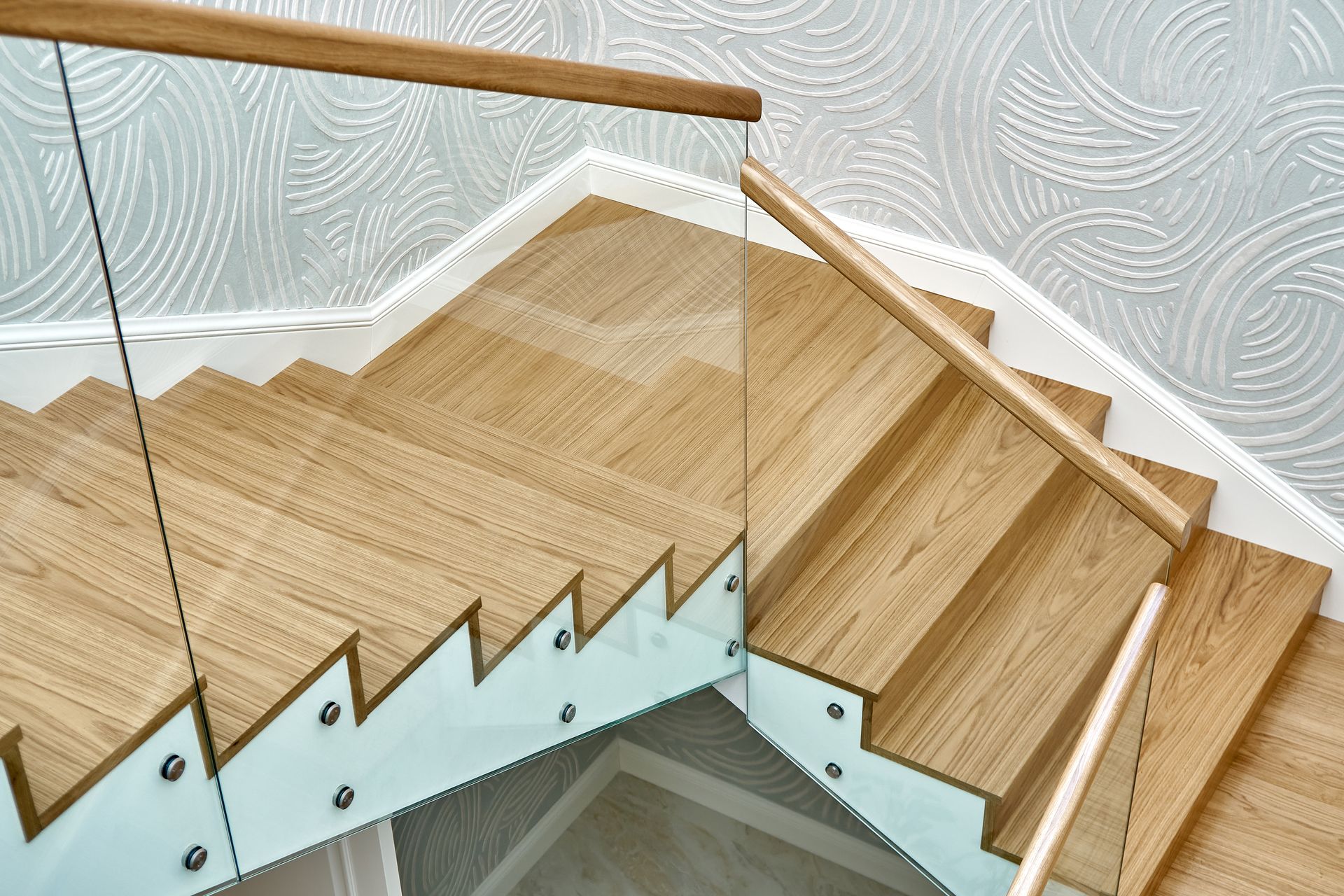 Wooden staircase with glass railing and patterned wallpaper on the landing