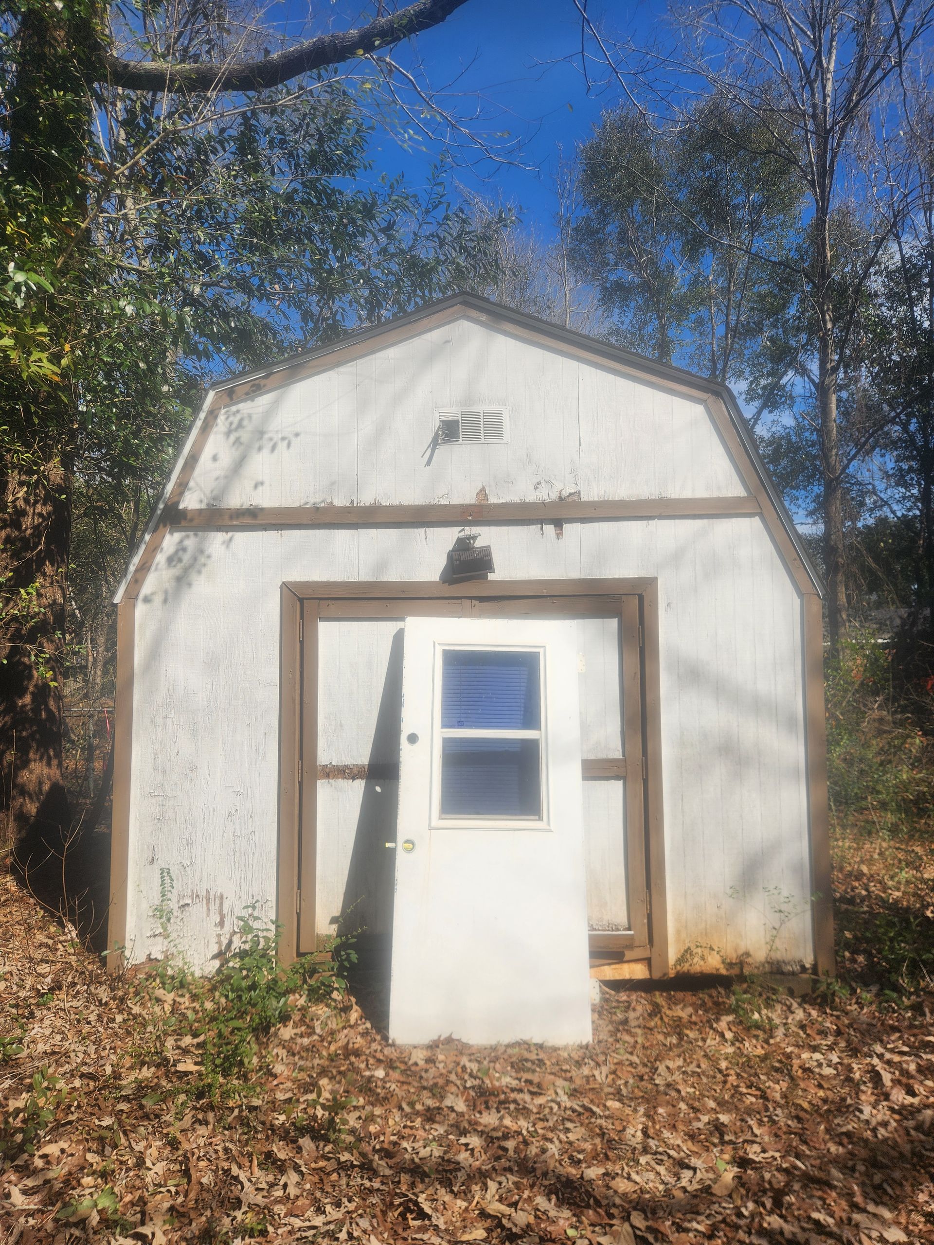 A white barn with a door and window is surrounded by trees.