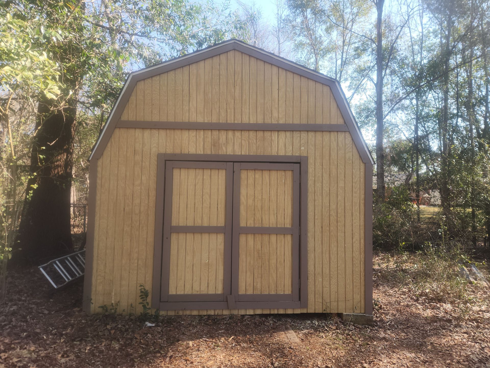 A wooden barn with two doors is sitting in the middle of a forest.