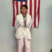 A woman in a karate uniform is standing in front of an american flag.
