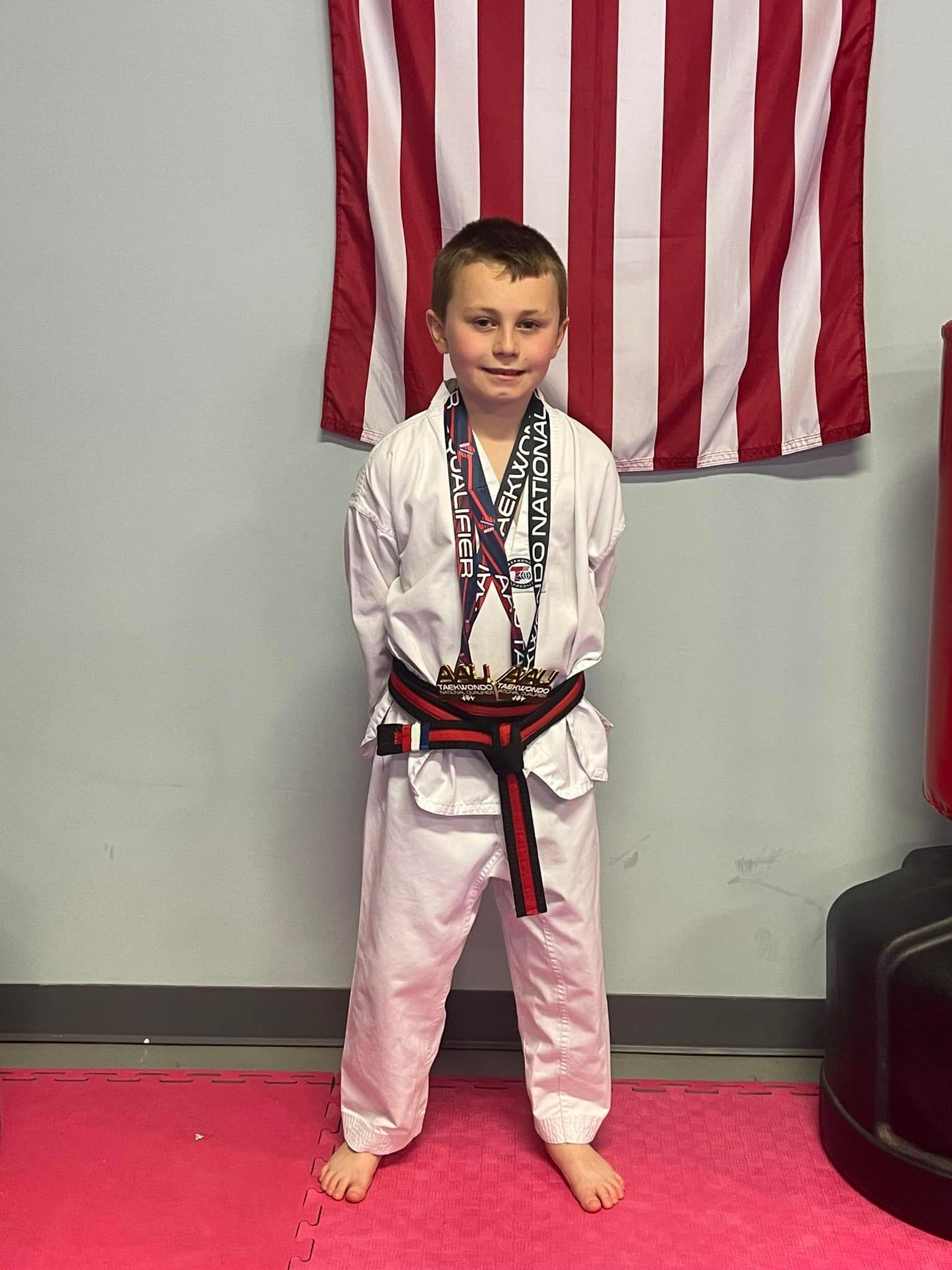 A young boy in a karate uniform is standing in front of an american flag.