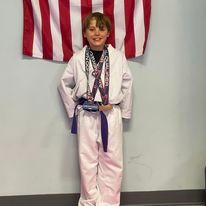 A young boy in a taekwondo uniform is standing in front of an american flag.