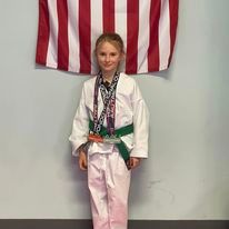 A young girl in a karate uniform is standing in front of an american flag.